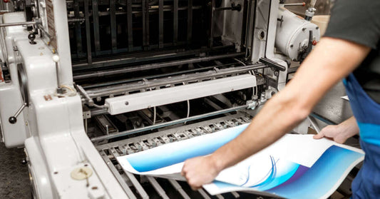 Printing process showing an operator handling colorful printed sheets from an industrial printing press.