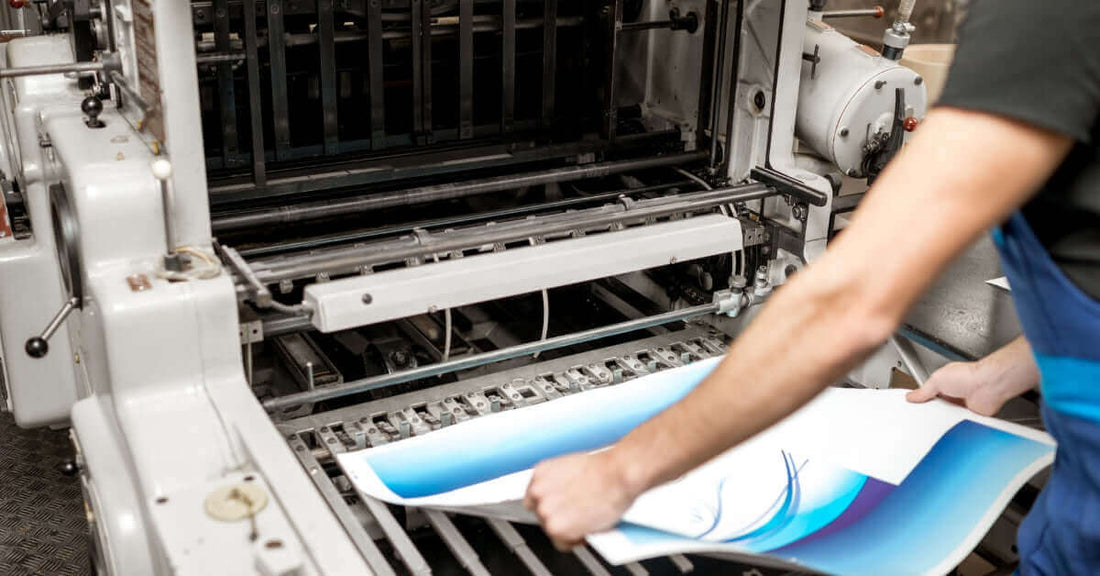 Printing process showing an operator handling colorful printed sheets from an industrial printing press.