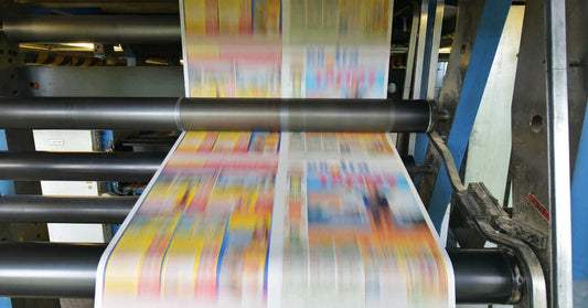 Close-up of a printing press with colorful flyers in motion, showcasing traditional printing in a digital era.